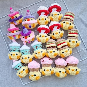 May include: A collection of handmade, yellow crochet chicks, each adorned with unique hats or accessories. Some chicks have cupcake-shaped toppers, while others sport colorful hats. The chicks are arranged on a white wire grid against a gray background.
