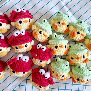 May include: A collection of crocheted stuffed animals, including yellow chicks with red crab and green frog hats. The animals are made with soft yarn and have embroidered eyes.