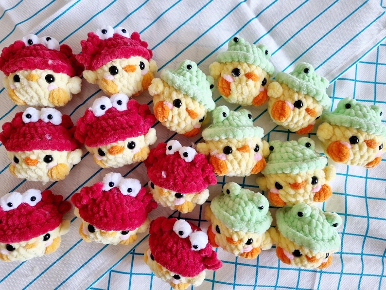 May include: A collection of crocheted stuffed animals, including yellow chicks with red crab and green frog hats. The animals are made with soft yarn and have embroidered eyes.