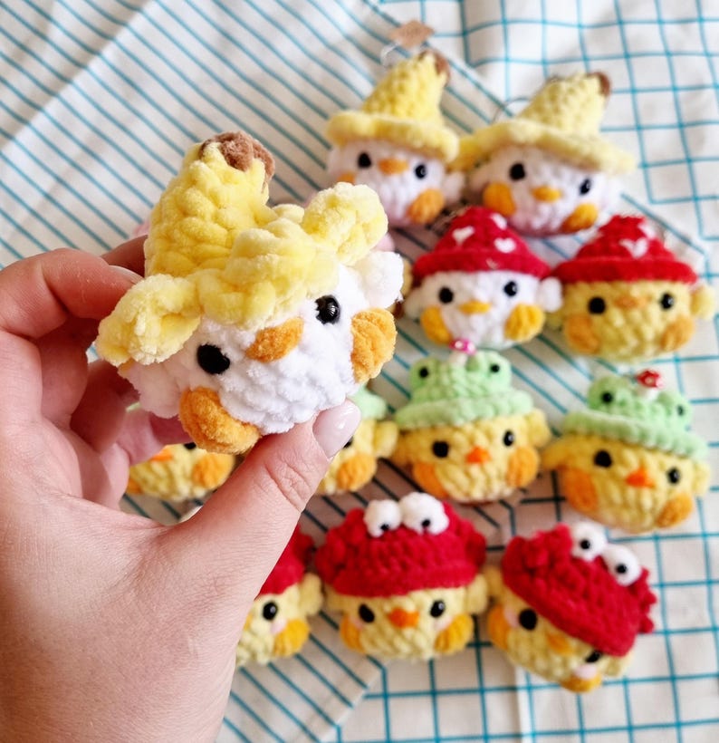 May include: A collection of crocheted chick ornaments with various toppings, including a banana, a mushroom, and a green hat. The chicks are all white with yellow beaks and black eyes.