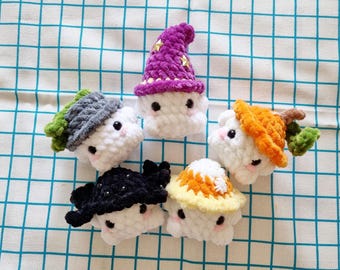 May include: Five crocheted stuffed animals with different colored hats. The hats include a purple witch hat, a green and gray hat, a black hat, a yellow and orange hat, and an orange pumpkin hat.