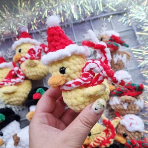 May include: Crocheted yellow duck ornaments wearing red Santa hats and striped scarves. The handmade ducks have black eyes and orange beaks. Some ducks are wearing black hats. Christmas-themed decorations.