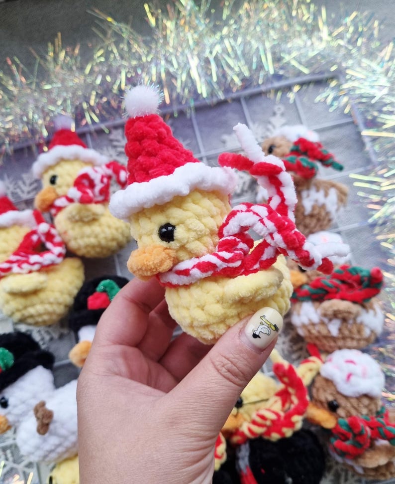 May include: Crocheted yellow duck ornaments wearing red Santa hats and striped scarves. The handmade ducks have black eyes and orange beaks. Some ducks are wearing black hats. Christmas-themed decorations.