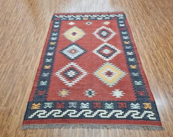 May include: A red, blue, and white patterned rug with a geometric design. The rug has a fringe border.
