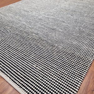 May include: Black and white striped rug with a textured surface. The rug has a subtle ombre effect, with the black stripes becoming more prominent towards the bottom.