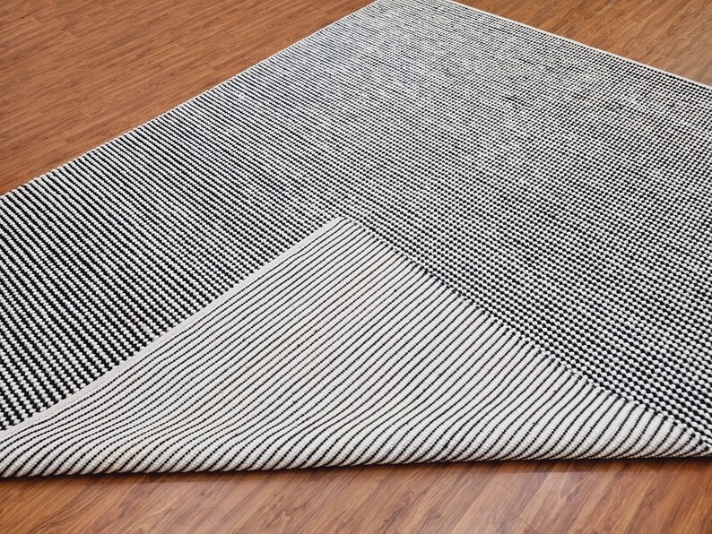 May include: A black and white striped rug with a geometric design. The rug is made of a soft, woven material and has a contemporary style.