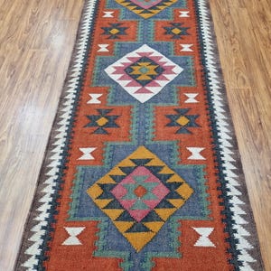 May include: A long, narrow rug with a geometric pattern in shades of red, blue, green, white, and black. The rug has a traditional, tribal design.