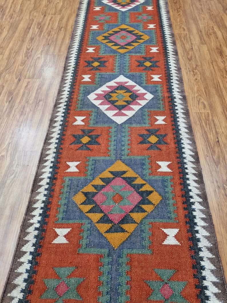 May include: A long, narrow rug with a geometric pattern in shades of red, blue, green, white, and black. The rug has a traditional, tribal design.