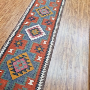 May include: A long, narrow rug with a geometric pattern in shades of red, blue, yellow, and white. The rug has a fringe on both ends.