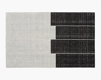 May include: A black and white striped rug with a geometric design. The rug has a white background with black vertical stripes on the left side and a black background with white horizontal stripes on the right side.