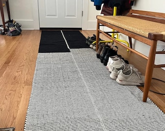 May include: A black and white patterned rug with a black and white striped rug underneath. A wooden bench with a woven seat is in the background with shoes underneath.