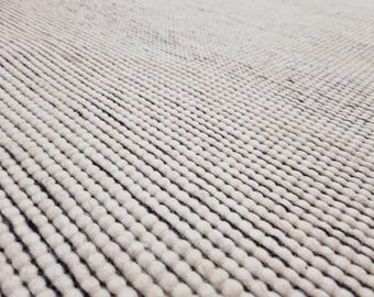 Puede incluir: Primer plano de una alfombra blanca texturizada con un patrón tejido. La alfombra tiene una textura suave y esponjosa y está hecha de fibras naturales.