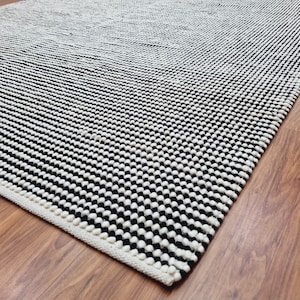 May include: A black and white patterned rug with a white border. The rug is made of a thick, textured material.
