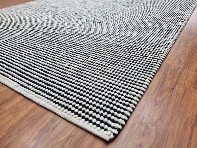 May include: A black and white patterned rug with a white border. The rug is made of a thick, textured material.