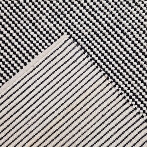 May include: Black and white striped rug with a geometric pattern. The rug is made of a soft, textured material.