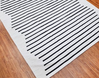 May include: A white and black striped rug with thin black stripes on a white background.