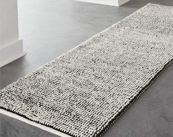 Puede incluir: Un tapete de corredor de diseño tejido con textura, en blanco y negro. El tapete está hecho de un material suave y mullido y tiene un brillo sutil.