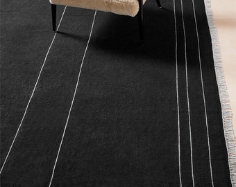 May include: Black area rug with white stripes. The rug has a fringe border.