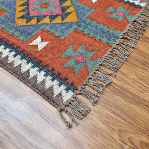 May include: A colorful rug with a geometric pattern in shades of red, orange, blue, green, and brown. The rug has a fringe border.