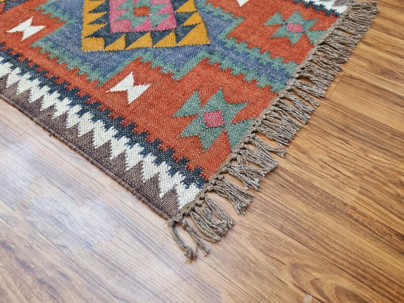 May include: A colorful rug with a geometric pattern in shades of red, orange, blue, green, and brown. The rug has a fringe border.