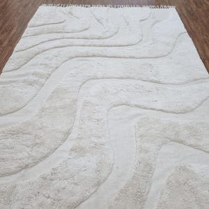May include: A white shag rug with a wavy, abstract design. The rug has a subtle texture and a fringe border.
