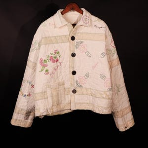 Puede incluir: Una chaqueta acolchada blanca con flores y texto bordados. El texto incluye "Love", "Morgan", "Babe" y "F.D. Rum Jr."