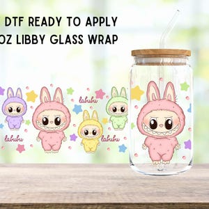 May include: A 16 oz glass tumbler with a straw and a pink bunny with a toothy grin design. The design also includes the text "labu bu" in pink and yellow. The tumbler is ready to be decorated with UV DTF.