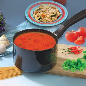 May include: A black saucepan with a black handle filled with red tomato sauce. The saucepan is on a blue surface next to a wooden chopping board with green onions, red chilli peppers, and red tomatoes.