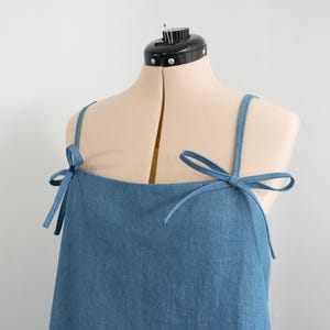 K&ouml;nnte beinhalten: Ein blaues, &auml;rmelloses Kleid aus Denim mit verstellbaren Tr&auml;gern, die an den Schultern zu Schleifen gebunden werden.