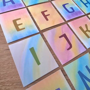 May include: A set of colorful cards with letters of the alphabet printed on them. Each card has a different color gradient and the letters are in a variety of colors.
