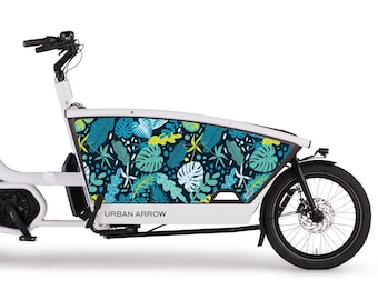 Pode incluir: Bicicleta de carga branca com roda dianteira e guiador pretos. O painel lateral apresenta um padrão de folhas tropicais em tons de azul, verde e branco. O texto "URBAN ARROW" está impresso na lateral.