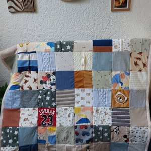 Puede incluir: Un edred&oacute;n de retazos hecho con cuadrados de tela variados. Los cuadrados presentan diferentes patrones, incluyendo estrellas, osos y Mickey Mouse. Algunos cuadrados est&aacute;n hechos de ropa, incluyendo una camiseta con "JORDAN 23". El edred&oacute;n est&aacute; sobre un sof&aacute;.