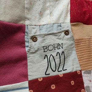 Puede incluir: Un edred&oacute;n de retazos compuesto por varios cuadrados de tela en tonos grises, rosas, rojos y blancos. Un cuadrado presenta el texto "BORN 2022" en negro. Otros cuadrados tienen patrones de corazones y flores.