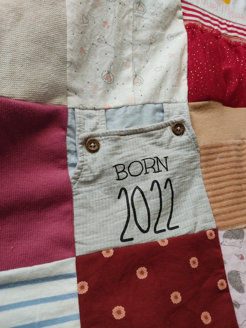Puede incluir: Un edred&oacute;n de retazos compuesto por varios cuadrados de tela en tonos grises, rosas, rojos y blancos. Un cuadrado presenta el texto "BORN 2022" en negro. Otros cuadrados tienen patrones de corazones y flores.