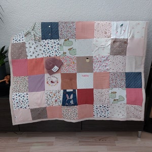 Puede incluir: Un edred&oacute;n de retazos en una variedad de colores pastel, incluyendo rosa, melocot&oacute;n y blanco, con un borde beige. El edred&oacute;n est&aacute; hecho de cuadrados de diferentes telas, algunos con estampados florales y otros con colores s&oacute;lidos. Un peque&ntilde;o gorro rosa con el texto "star kakao" encima.