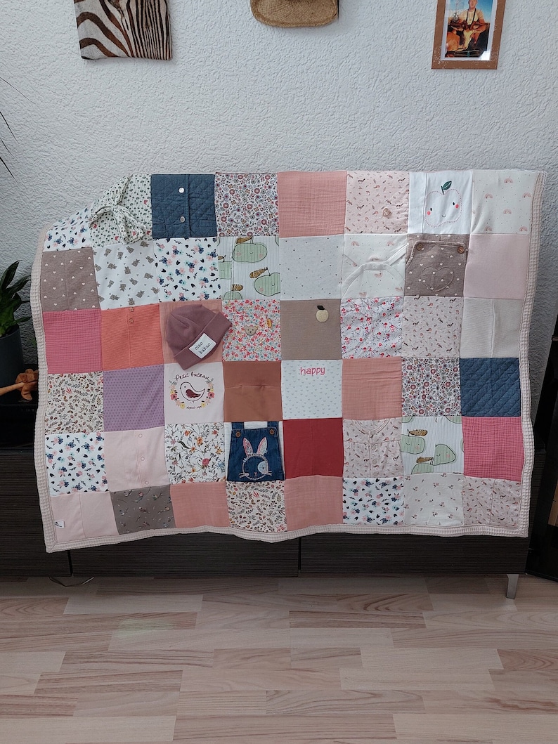 Puede incluir: Un edred&oacute;n de retazos en una variedad de colores pastel, incluyendo rosa, melocot&oacute;n y blanco, con un borde beige. El edred&oacute;n est&aacute; hecho de cuadrados de diferentes telas, algunos con estampados florales y otros con colores s&oacute;lidos. Un peque&ntilde;o gorro rosa con el texto "star kakao" encima.