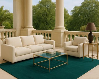 May include: A cream-colored three-seat sofa and a matching armchair are arranged on a large, solid dark teal area rug. A rectangular coffee table with a glass top and gold metal frame sits between them, alongside a matching side table.