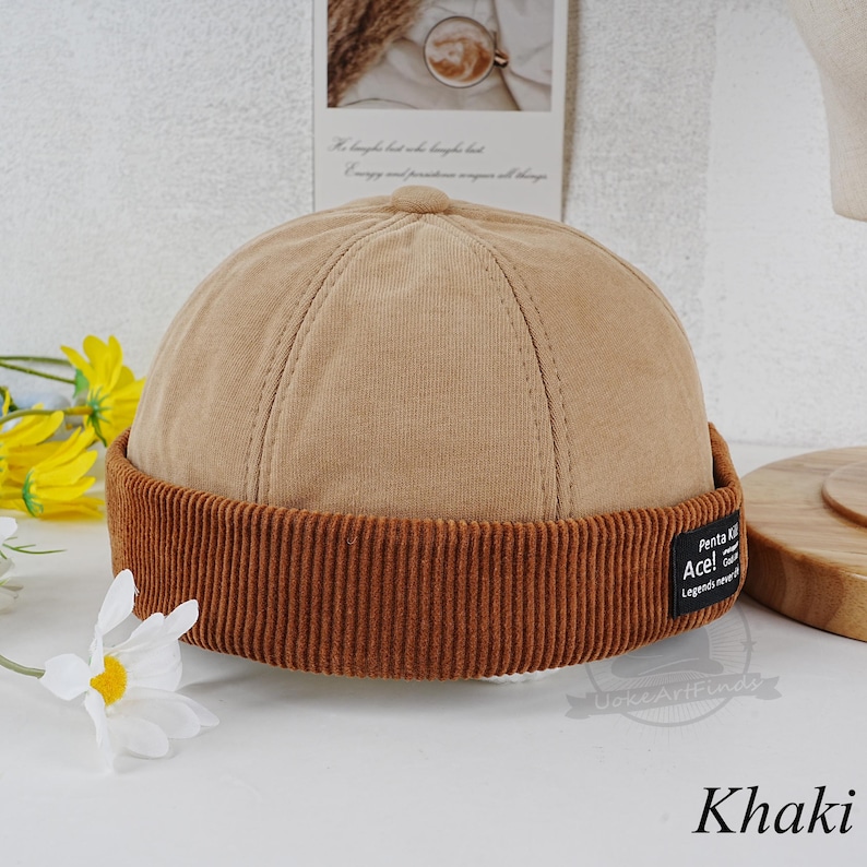 Może przedstawiać: Beanie w kolorze khaki z brązowym, welurowym rondem. Beanie ma czarną metkę z tekstem "Penta KI Ace! Legends never die".