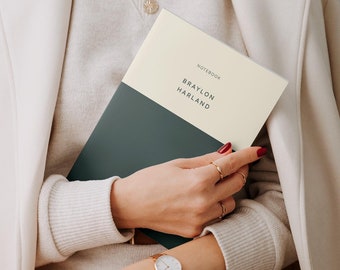 Könnte beinhalten: Eine Frau hält ein dunkelgrünes und cremefarbenes Notizbuch mit dem Text "NOTEBOOK BRAYLON HARLAND" auf dem Einband.