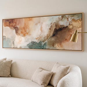 May include: A large, horizontal rectangular canvas painting featuring abstract swirls of warm beige, deep brown, soft cream, and muted teal tones. The artwork is encased in a light-colored wooden frame and is displayed on a plain white wall.