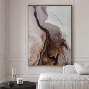 May include: A large rectangular wall art piece featuring an abstract fluid design with swirling shades of dark brown, beige, and white. The artwork is framed in a thin wood border and hangs on a white wall above a white sofa and a black coffee table.