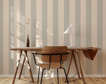 May include: A wooden desk with a black metal chair and a white lamp. The desk has a light brown wood top and two wooden legs. The chair has a light brown wood seat and a black metal frame. The lamp has a white shade and a black base. The wall behind the desk is covered in beige and gray striped wallpaper.