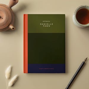 Könnte beinhalten: Ein grünes und blaues Notizbuch mit dem Text "NOTEBOOK DANIELLE FAWN" und "ELITE JOURNAL NYC" auf dem Cover.