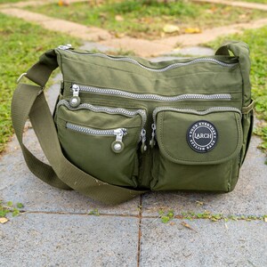 May include: A green nylon crossbody bag with multiple zippered pockets and a black patch with the text "YOUR EVERYDAY STYLISH BAG LARCH" in white.