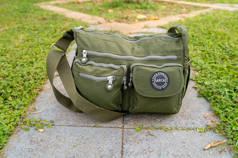 May include: A green nylon crossbody bag with multiple zippered pockets and a black patch with the text "YOUR EVERYDAY STYLISH BAG LARCH" in white.