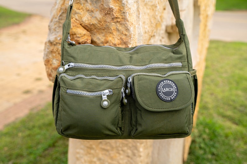 May include: A green crossbody bag with multiple zippered pockets and a black circular patch that reads "Your Everyday Stylish Bags LARCH".