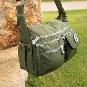 May include: A green nylon shoulder bag with multiple zippered compartments and a small pocket with a circular logo.