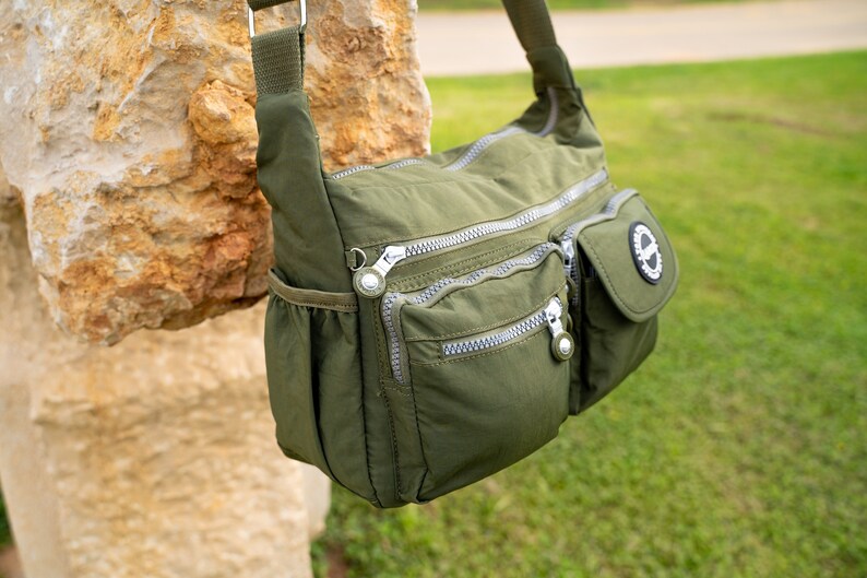 May include: A green nylon shoulder bag with multiple zippered compartments and a small pocket with a circular logo.