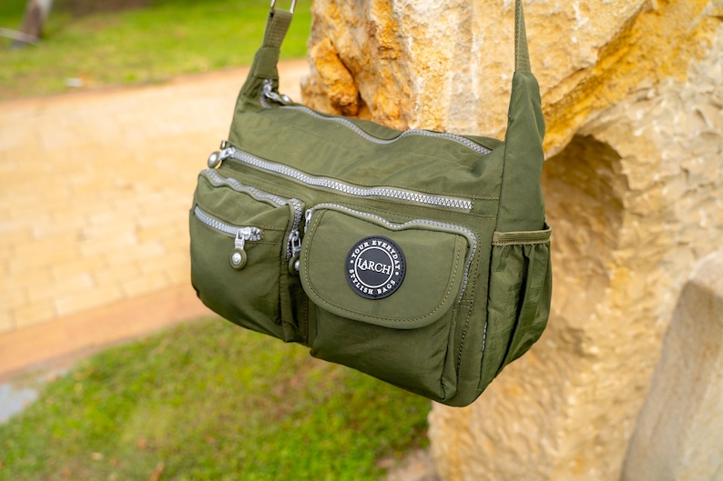 May include: A green nylon shoulder bag with multiple zippered compartments and a large front pocket with a black circular patch that reads "Your Everyday Stylish Bags LARCH".