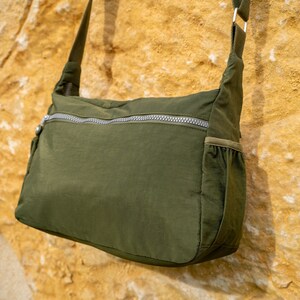 May include: A dark green crossbody bag with a zippered pocket and a small pocket on the side. The bag is made of a soft, lightweight material.